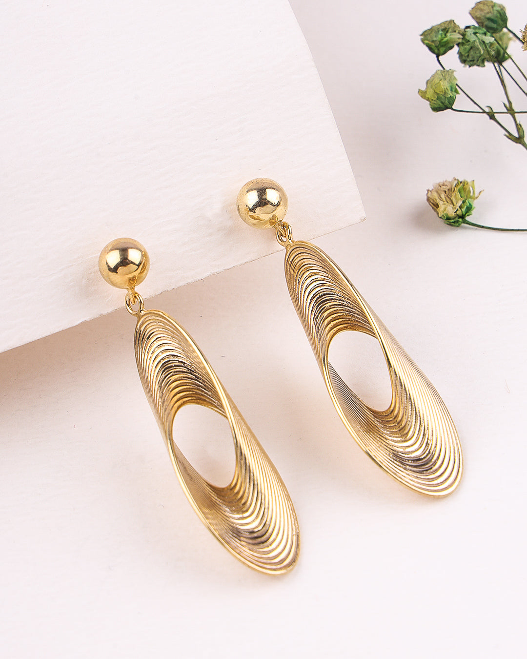 Gold earrings on a white surface with a blurred background
