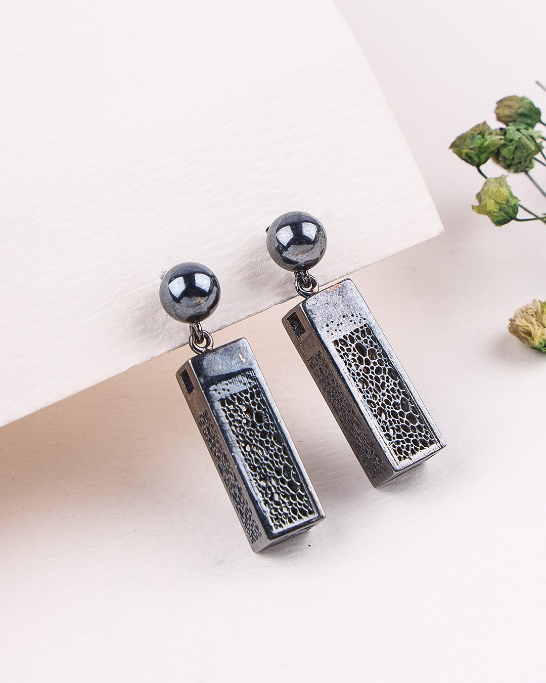 Pair of earrings with textured rectangular pendants and spherical tops on a light background.