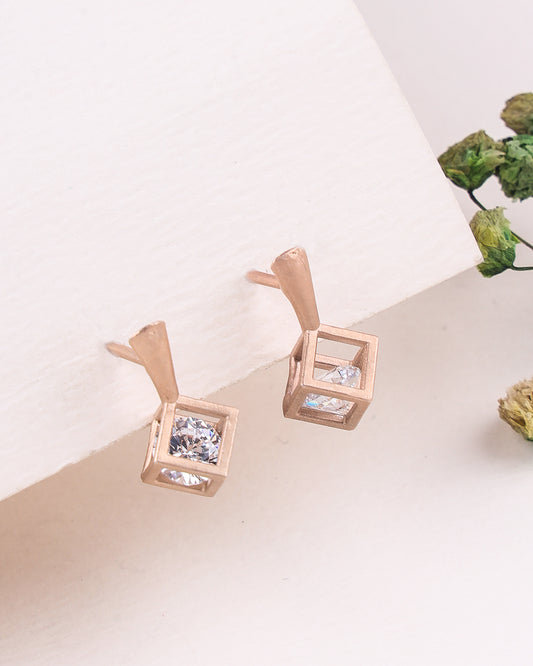 Rose gold earrings with clear gemstones on a light surface with greenery.