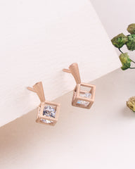 Rose gold earrings with clear gemstones on a light surface with greenery.