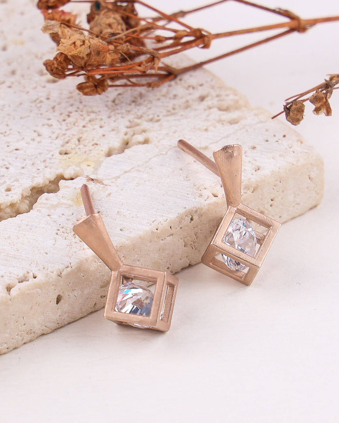 Rose gold square earrings with clear gemstones on a light stone surface.