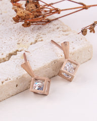 Rose gold square earrings with clear gemstones on a light stone surface.