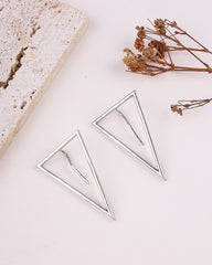 Pair of silver triangle earrings on a light surface with dried flowers.
