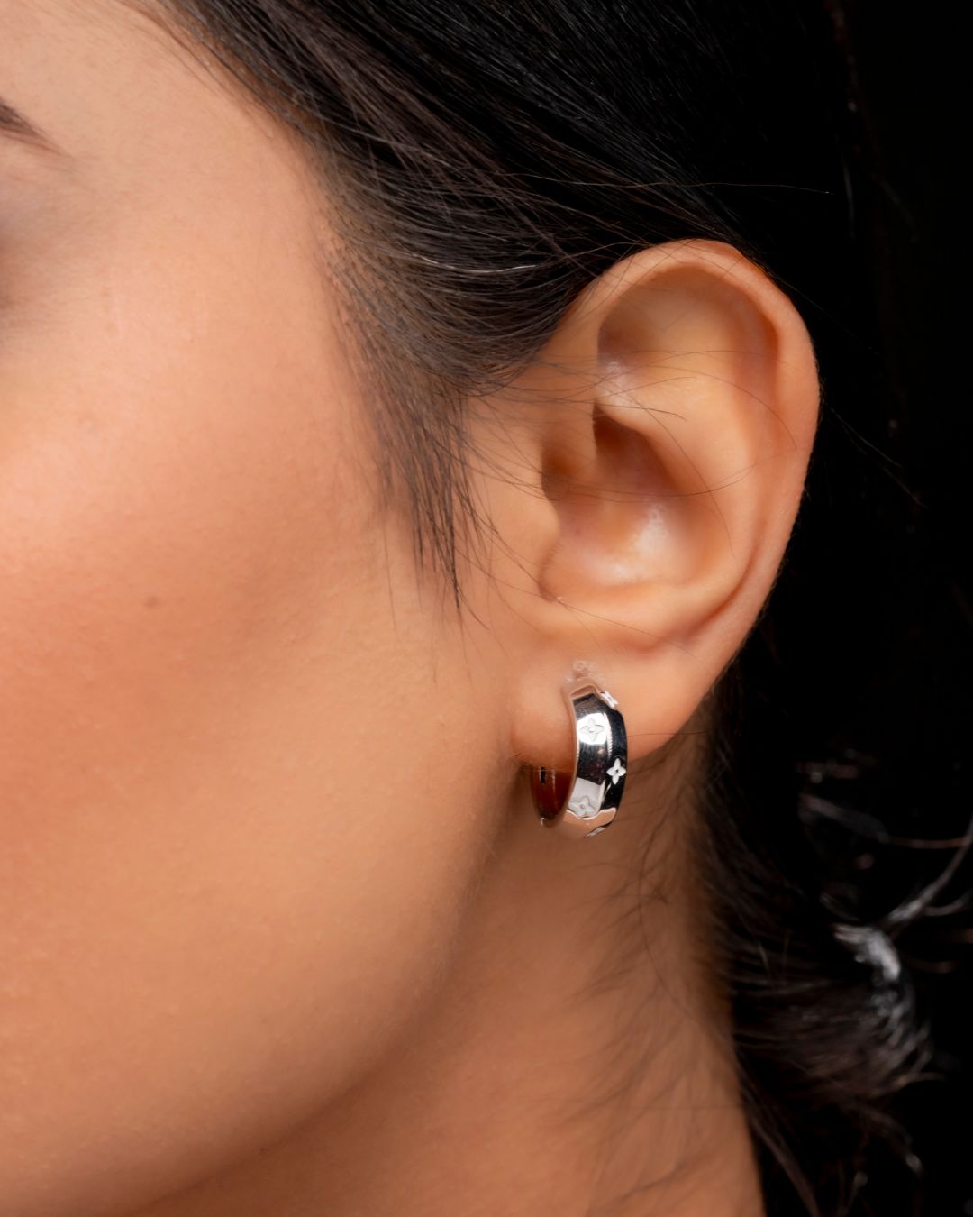 Close-up of an ear wearing a silver hoop earring with a blurred background