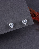 Heart-shaped stud earrings on a dark gray surface with a blurred red flower in the background.