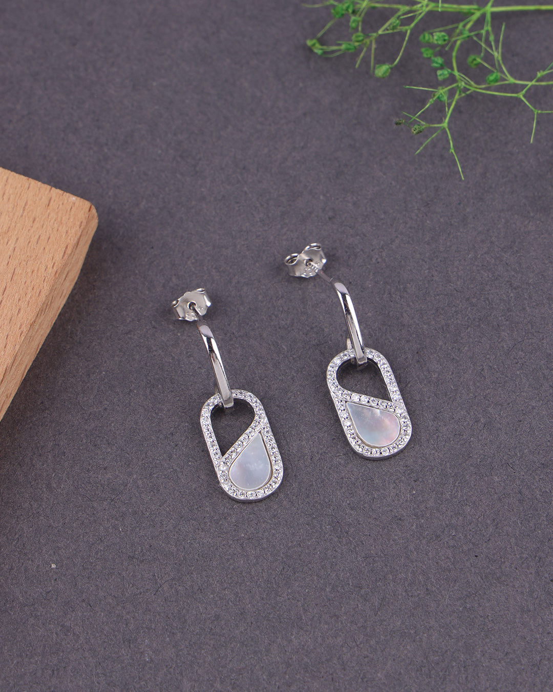Silver earrings with MOP on a dark surface with greenery