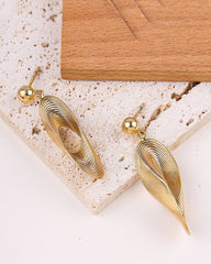 Gold earrings on a textured surface with a wooden block in the background