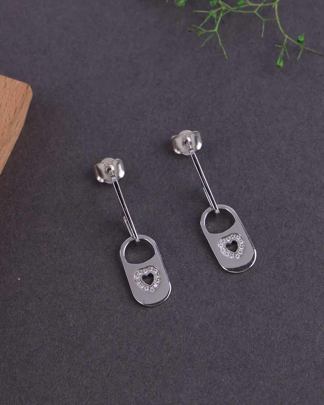 Pair of silver earrings with heart designs on a dark surface.