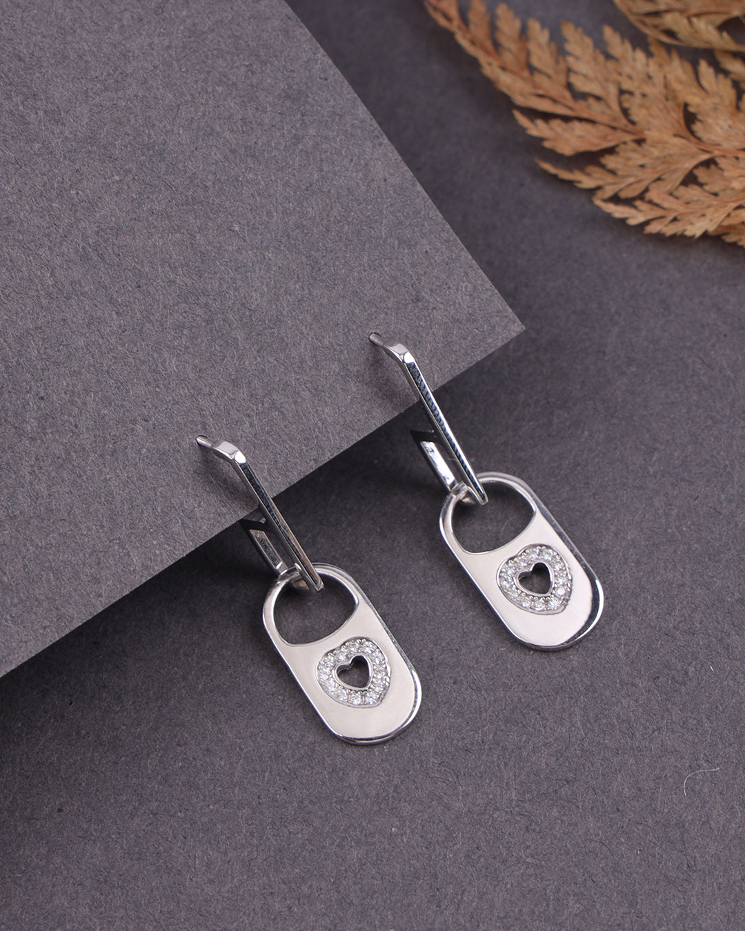 Silver earrings with heart designs on a gray surface