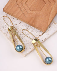 Gold plated earrings with blue spherical beads on a light stone surface.