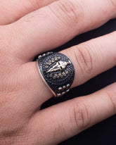 Silver ring with intricate design on a finger against a dark background