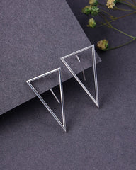 Pair of geometric silver earrings on a dark gray surface with dried flowers.