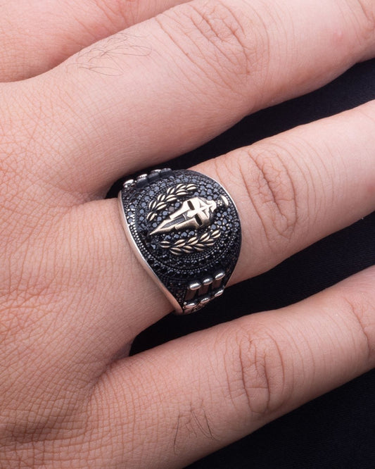 Silver ring with intricate design on a finger against a dark background