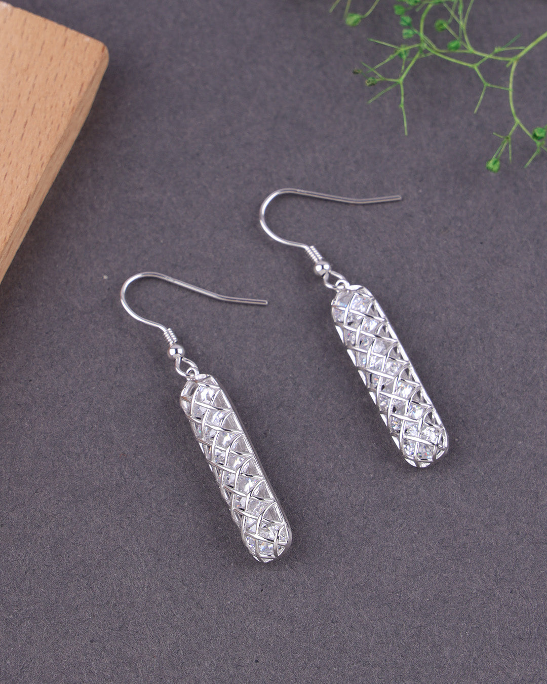 Silver earrings on a dark surface with a wooden block and green leaves in the background
