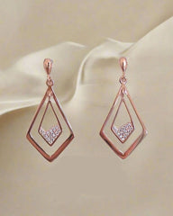 Rose gold earrings with diamond-like stones on a beige fabric background