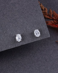 Pair of silver oval stud earrings on a dark gray surface with dried leaves.