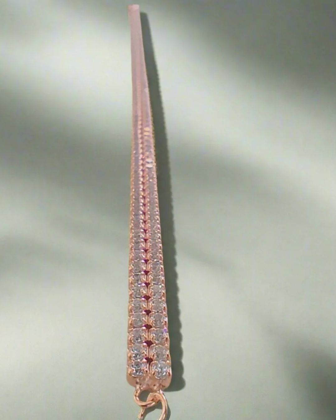 Rose gold bracelet with clear stones on a light gray background