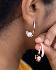 Close-up of a person wearing gold hoop earrings with pearls, holding one earring.