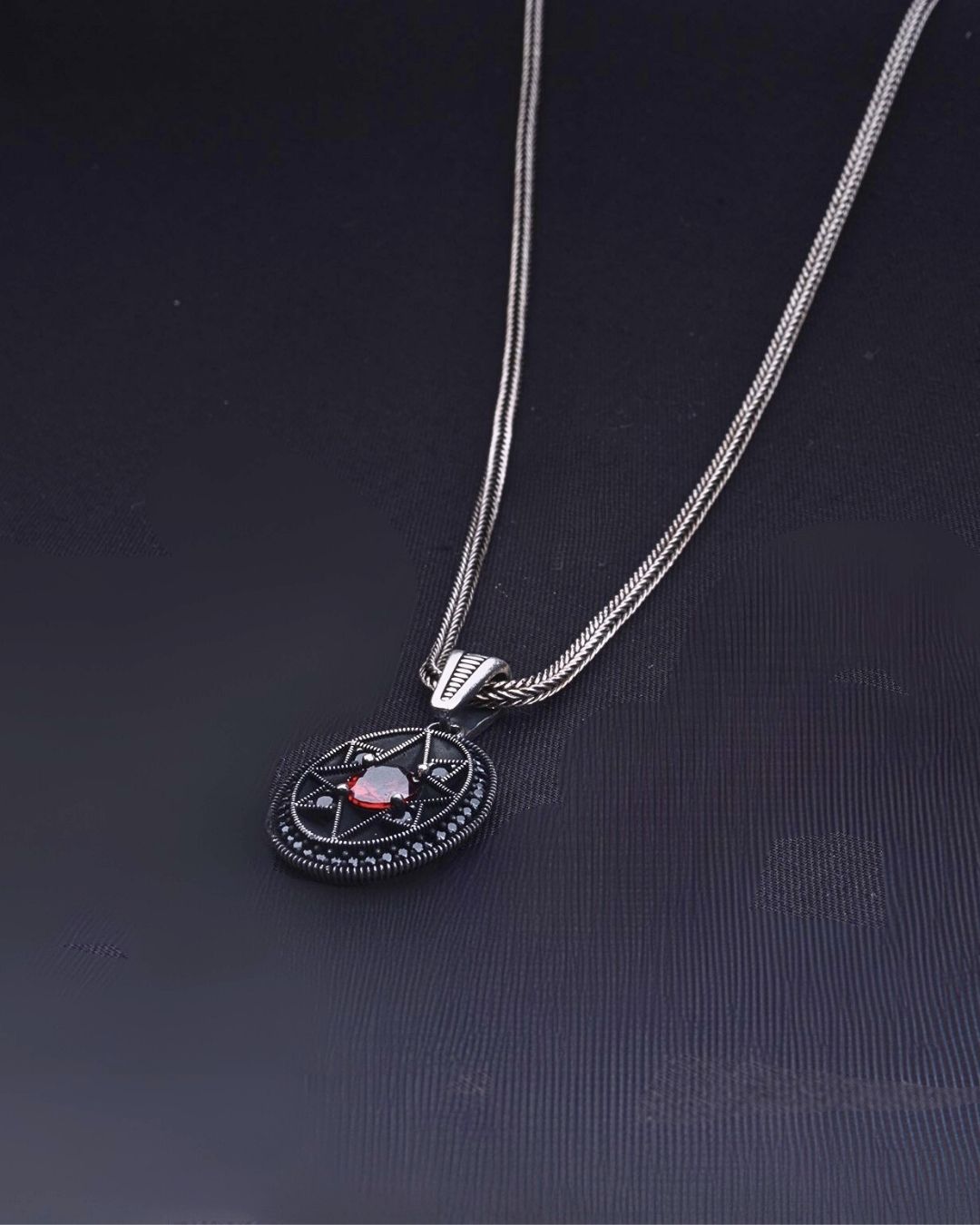 Silver necklace with a pendant featuring a red gemstone on a dark background