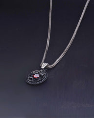Silver necklace with a pendant featuring a red gemstone on a dark background