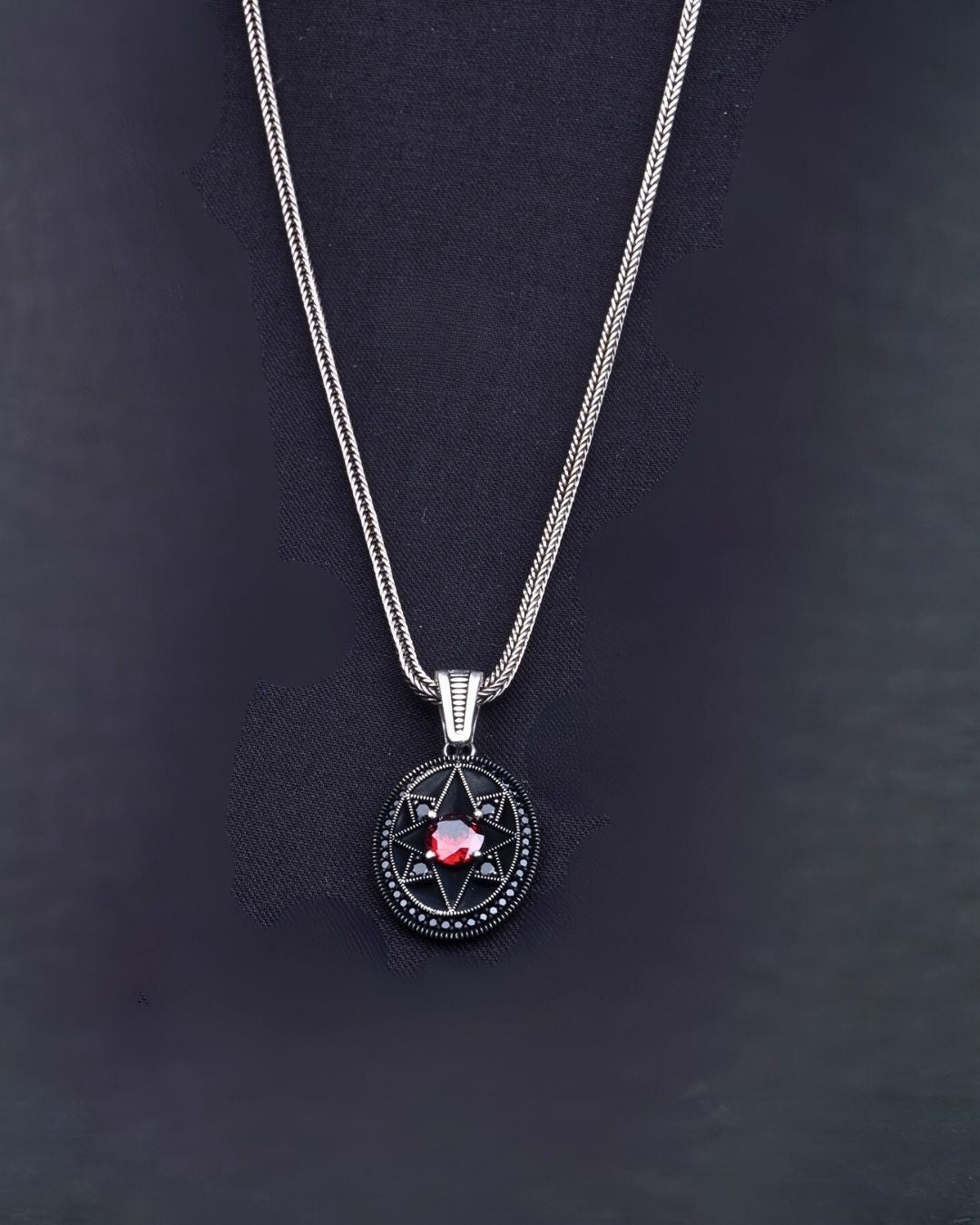 Silver necklace with a circular pendant featuring a red gemstone on a dark background