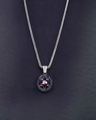 Silver necklace with a circular pendant featuring a red gemstone on a dark background