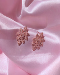 Rose gold leaf-shaped earrings on a pink fabric background