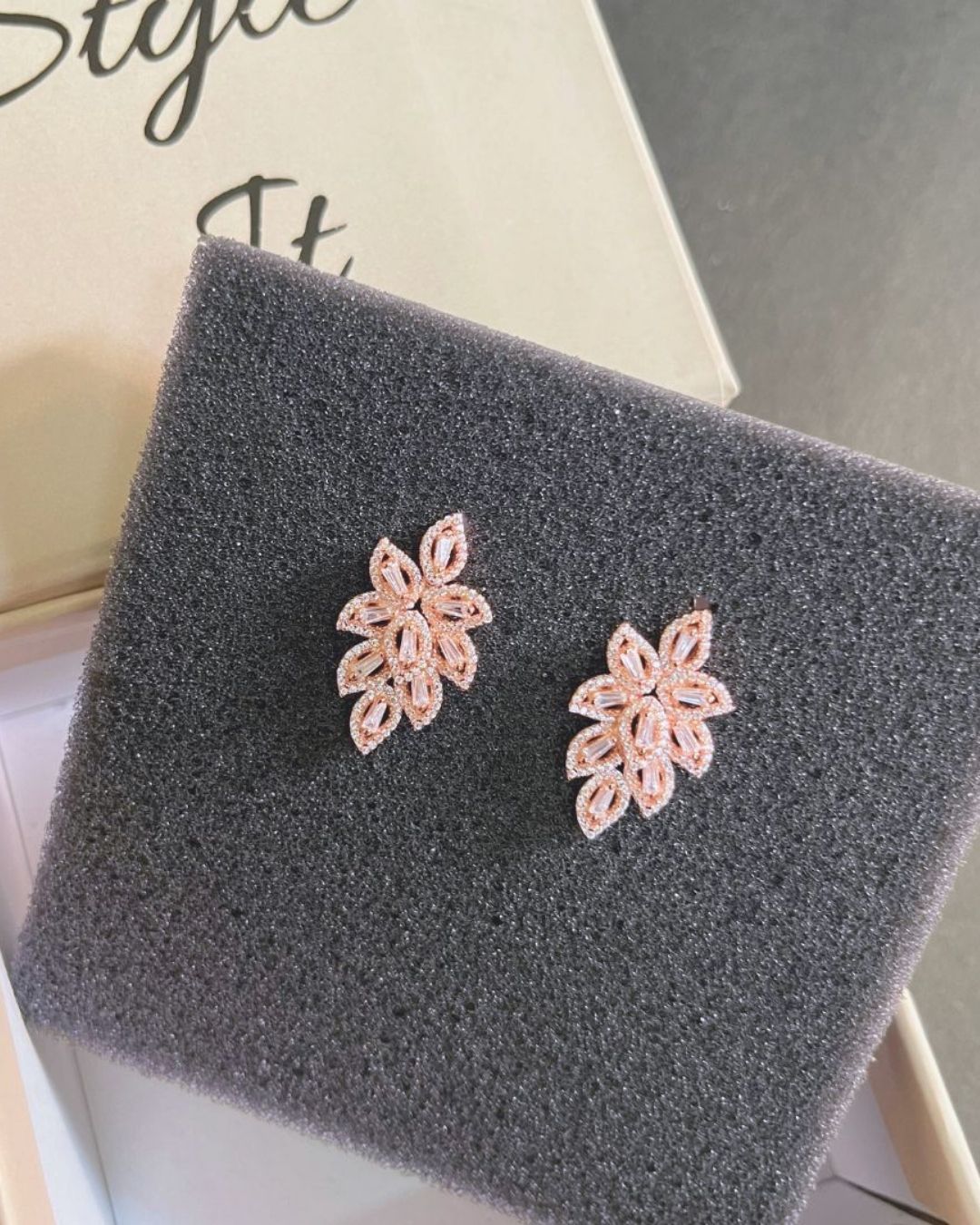 Pair of pink floral earrings on a gray textured surface.