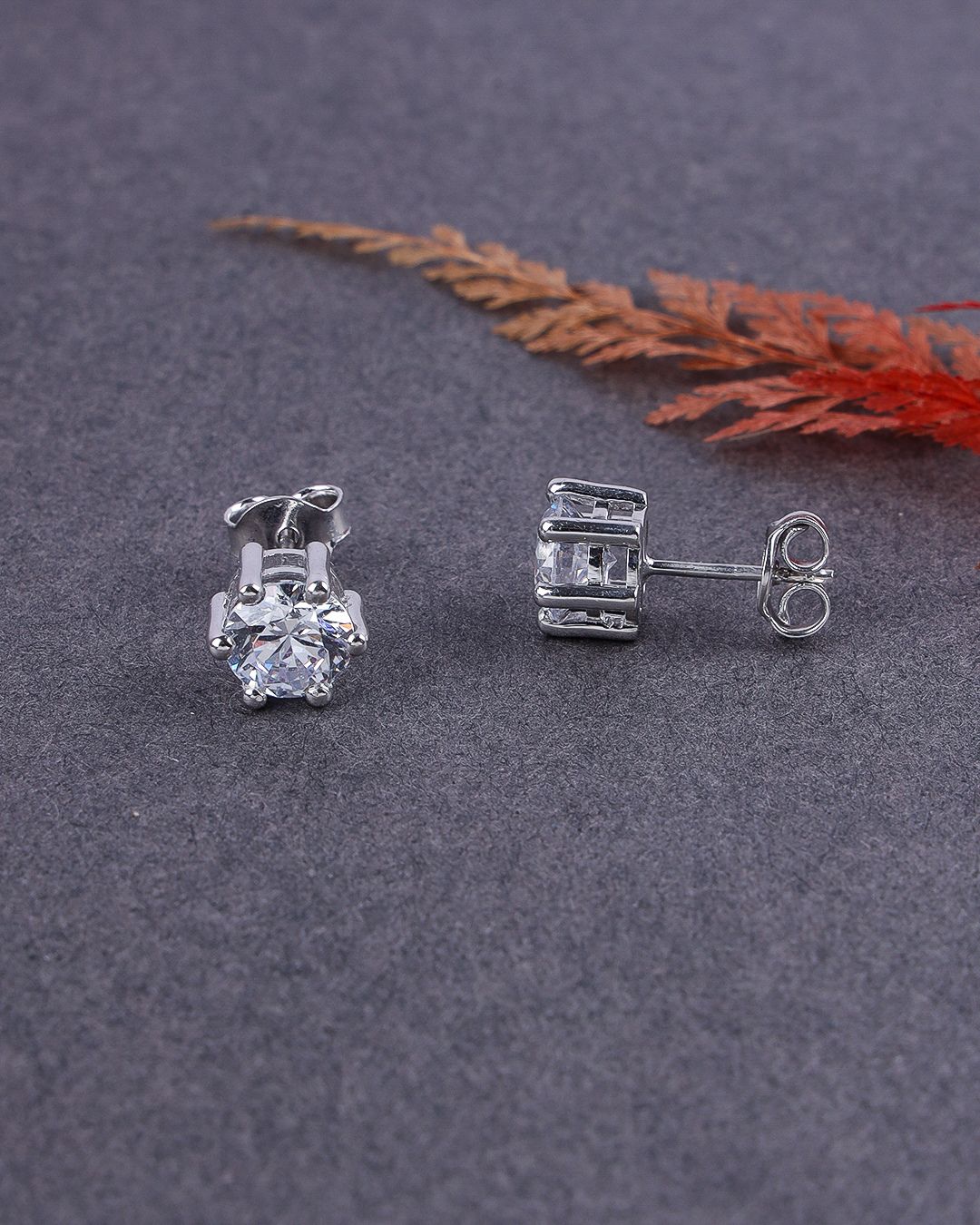 Silver stud earrings on a gray surface with a dried leaf in the background
