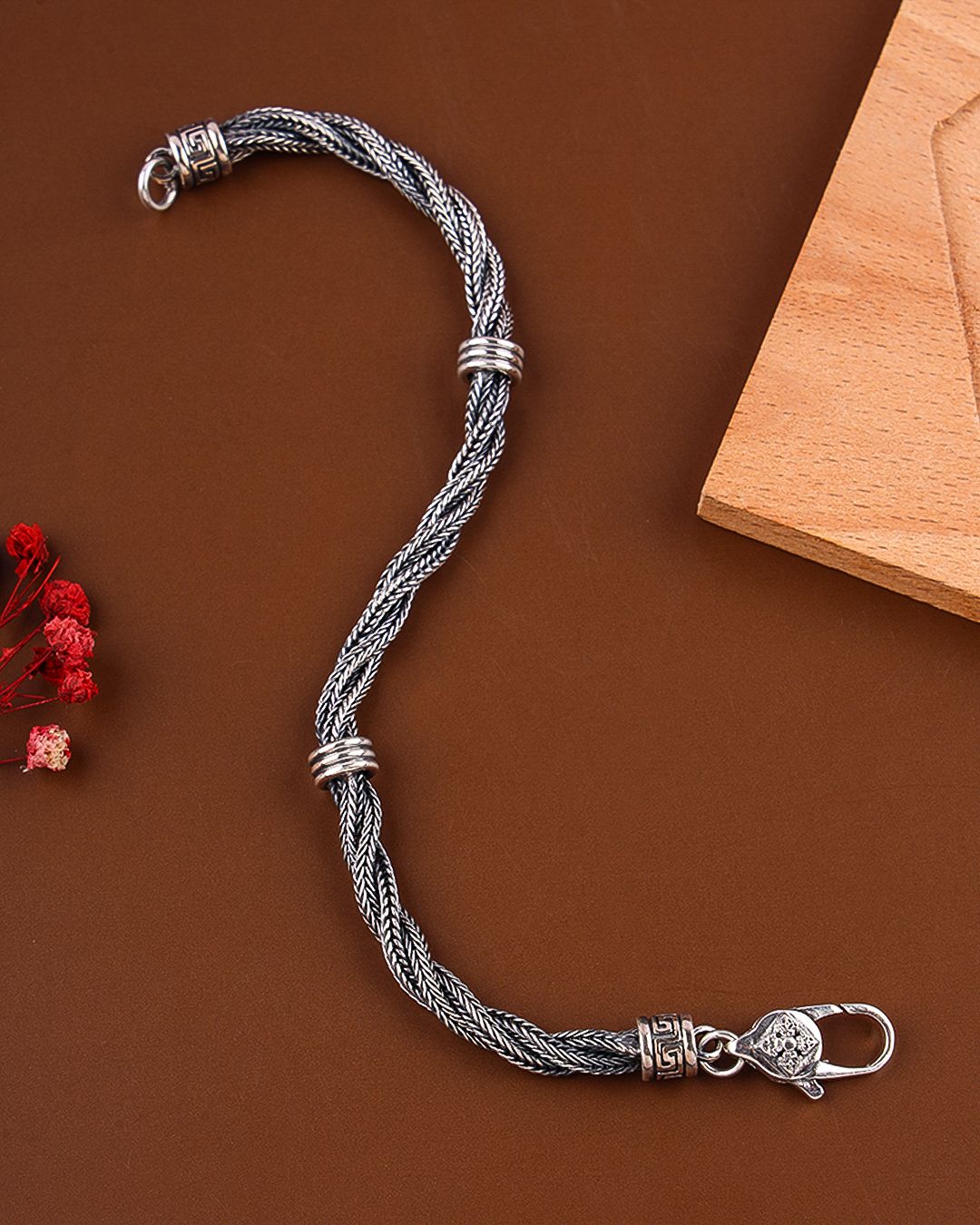 Silver braided bracelet with decorative clasp on a brown background