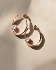Rose gold hoop earrings with clear gemstones on a beige background