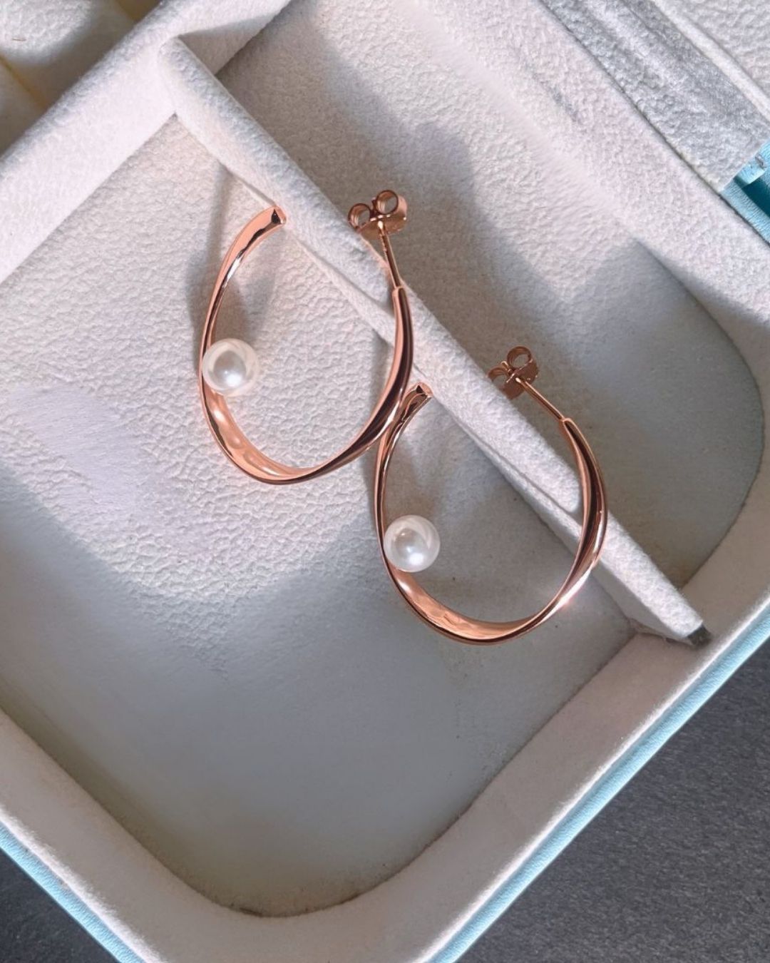 Rose gold hoop earrings with pearls on a white jewelry box