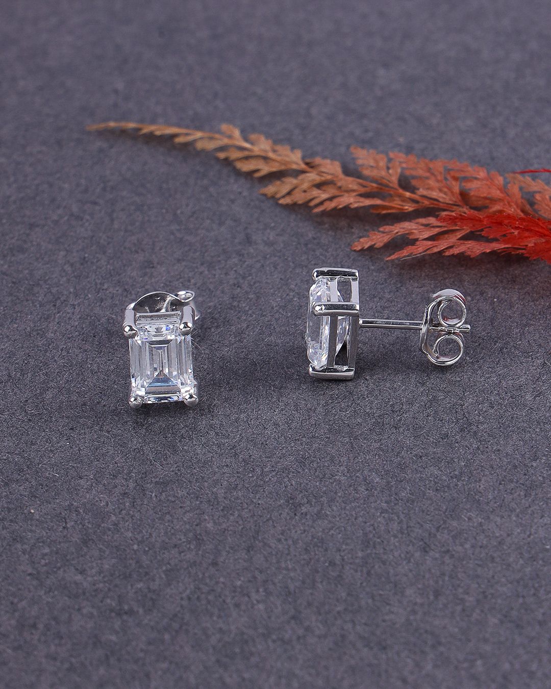 Silver earrings with rectangular gemstones on a dark surface with a red leaf.