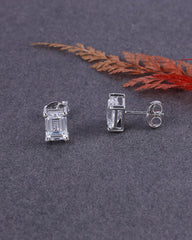 Silver earrings with rectangular gemstones on a dark surface with a red leaf.