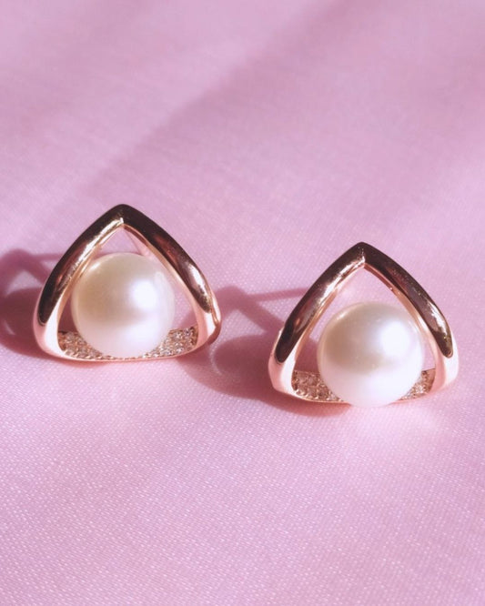 Pair of pearl earrings with gold triangular frames on a pink background