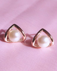 Pair of pearl earrings with gold triangular frames on a pink background