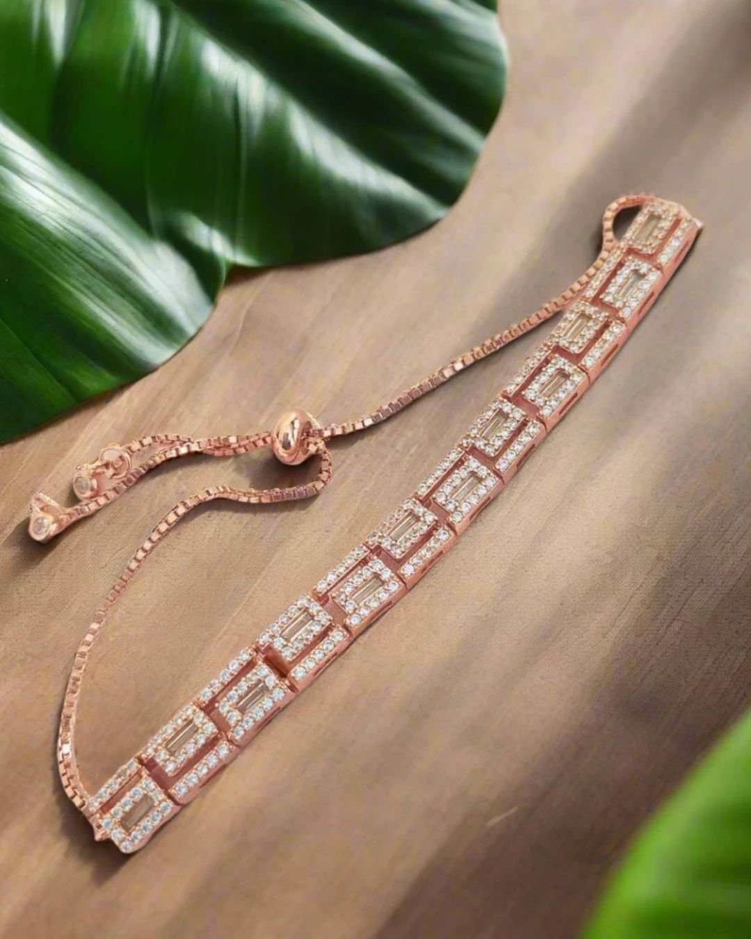 Rose gold bracelet with diamonds on a wooden surface with green leaves