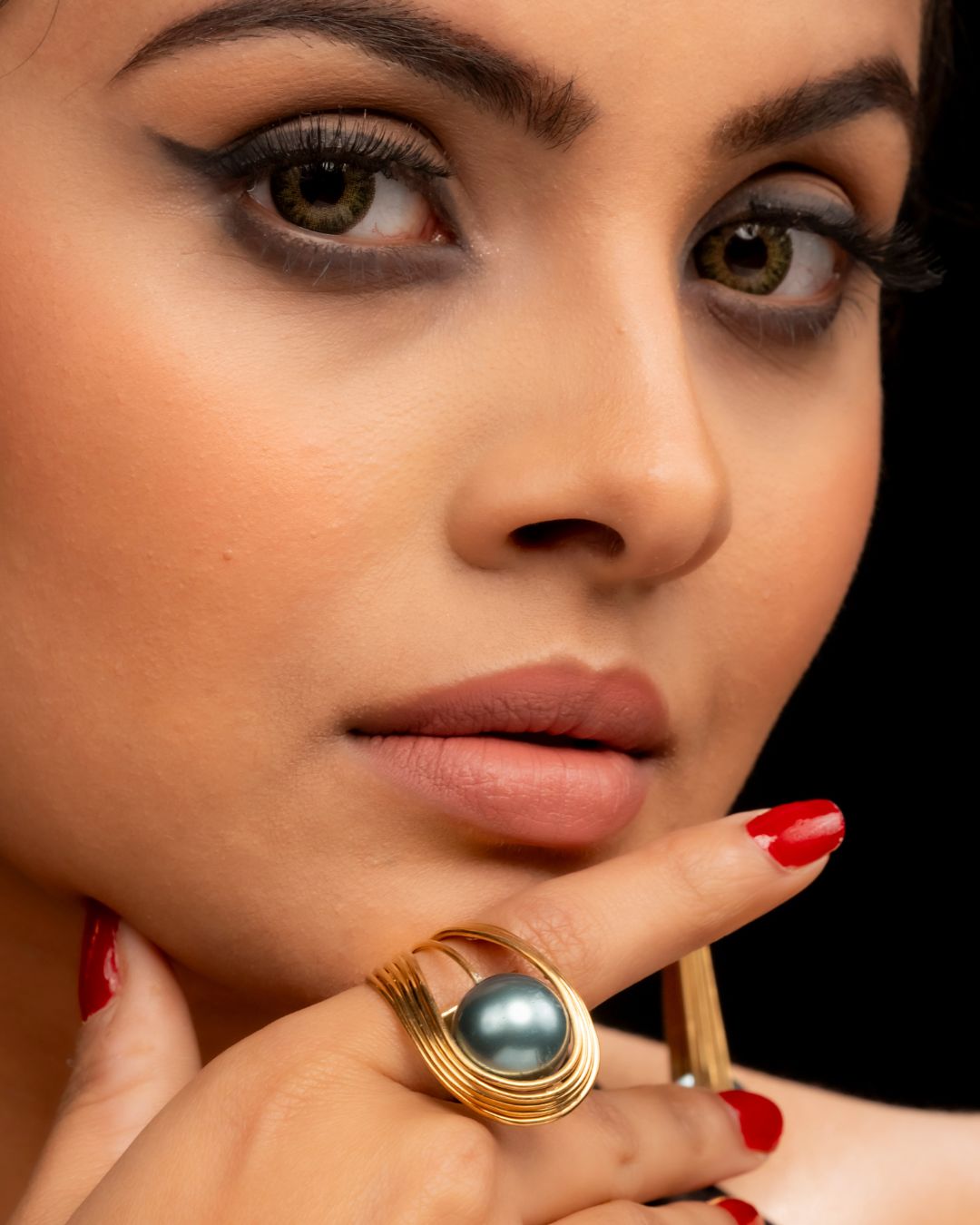 Close-up of a woman's face with makeup and a gold ring with a pearl.