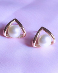 Pair of gold triangle-shaped earrings with pearl centers on a light purple background