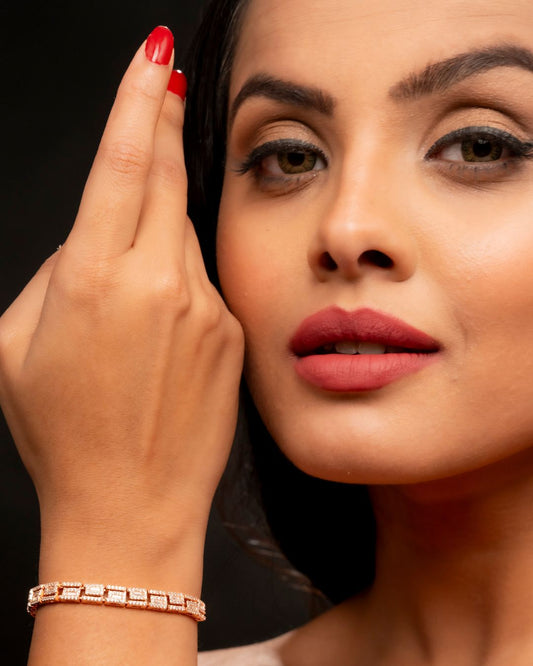 Close-up of a woman with red nail polish and a rose gold bracelet on a dark background