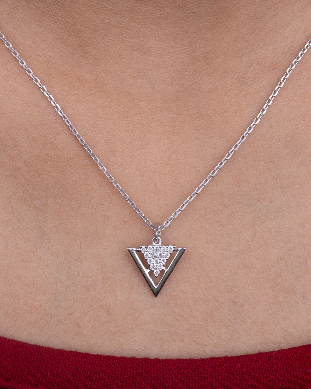 Silver necklace with a triangular pendant on a person wearing a red top.