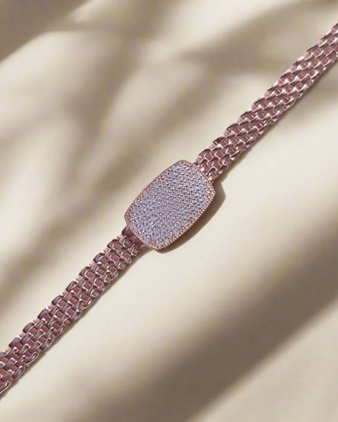Rose gold bracelet with diamond-encrusted clasp on a beige fabric background