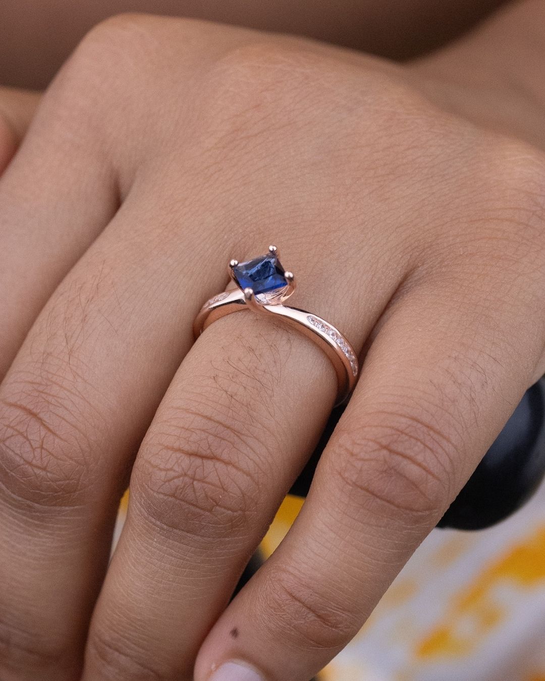 Rose gold ring with a blue gemstone on a finger