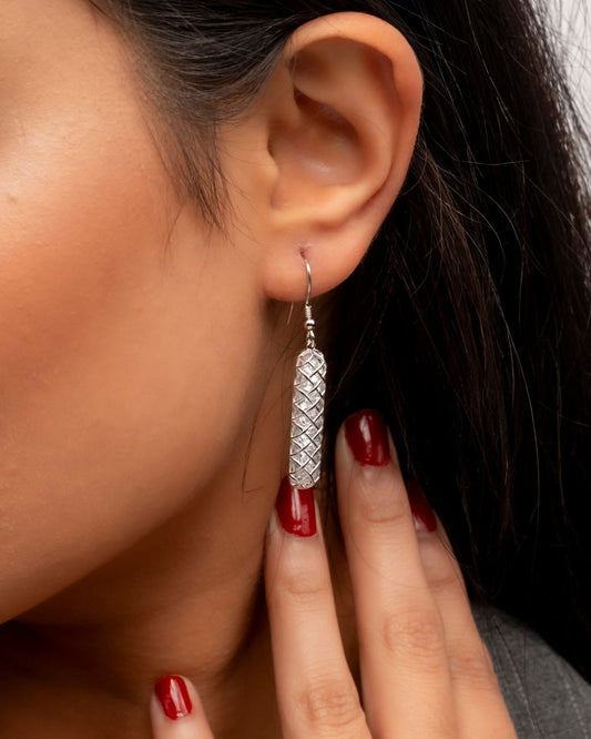 Close-up of an ear wearing a silver earring with a textured design, held by a hand with red nail polish.
