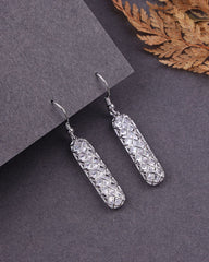 Silver earrings with a textured design on a dark surface with a leafy background