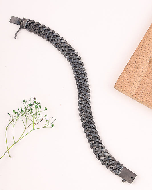 Gray braided bracelet on a white background with a wooden block and plant.