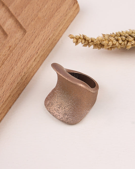 Rose gold silver ring on a light surface with wooden block and dried plant in background