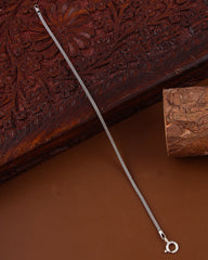 Silver bracelet on a textured brown surface with a wooden block in the background