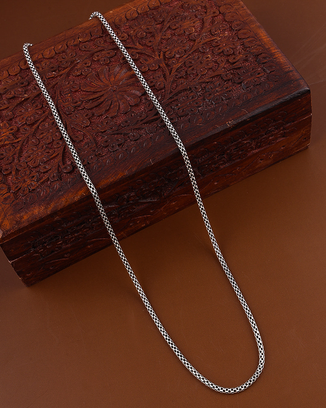 Silver chain on a wooden box with intricate carvings on a brown background