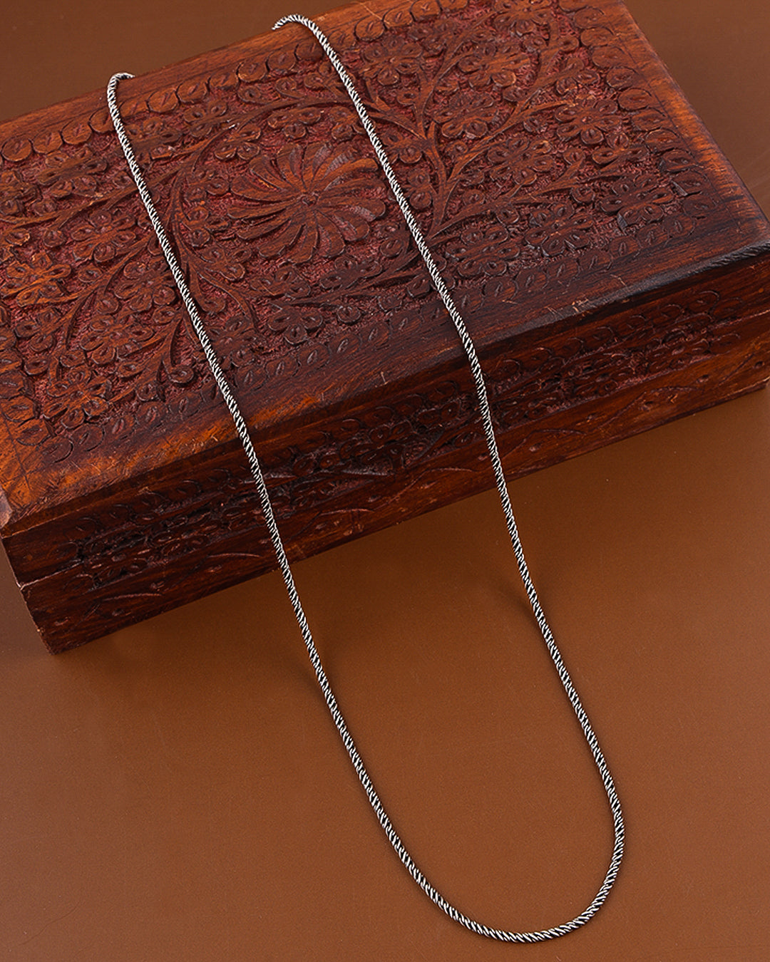 Silver chain on a wooden box with intricate carvings on a brown background